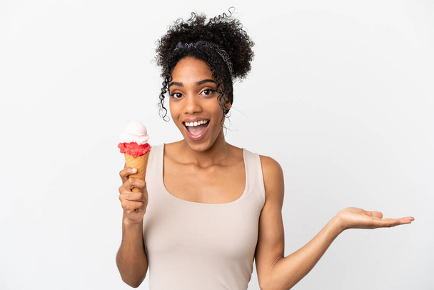 ショックを受けた顔の表情で白い背景に隔離されたコーンアイスクリームを持つ若いアフリカ系アメリカ人女性 - 写真・画像