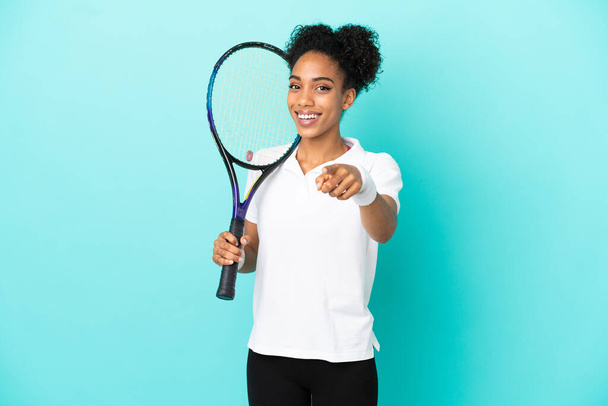 Genç tenisçi kadın mavi arka planda izole edilmiş, mutlu bir ifadeyle ön tarafı işaret ediyor. - Fotoğraf, Görsel