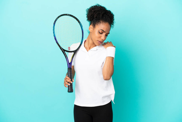 肩の痛みに苦しむ青い背景に孤立した若いテニス選手の女性の努力 - 写真・画像