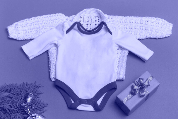 Christmas white baby bodysuit mockup on very peri background close up - with knitted white jacket - mockup of newborn clothes. With copy space. Monochrom - Photo, Image