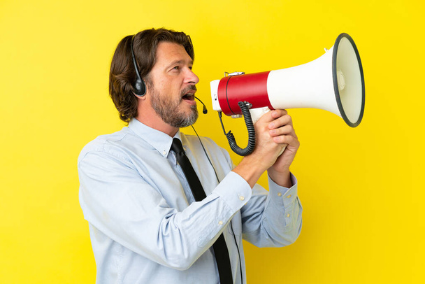 Hombre holandés telemarketer trabajando con un auricular aislado sobre fondo amarillo gritando a través de un megáfono - Foto, imagen