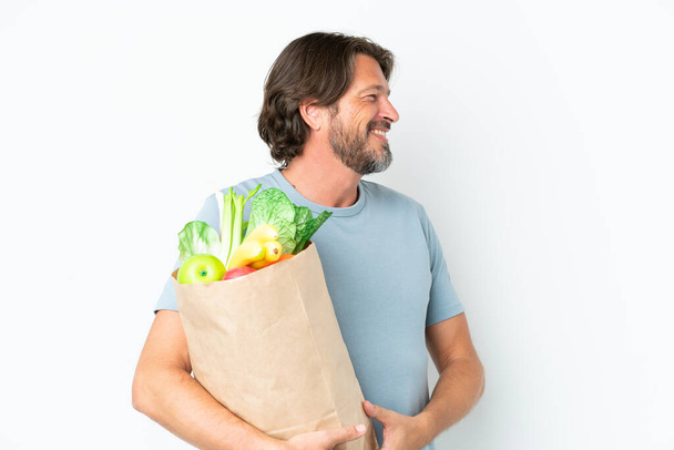 Senior dutch man holding grocery shopping bag over isolated background looking side - Foto, Imagem
