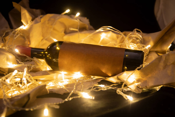 wine bottle with blank label lies in shining golden garland. mockup copy space - Fotó, kép