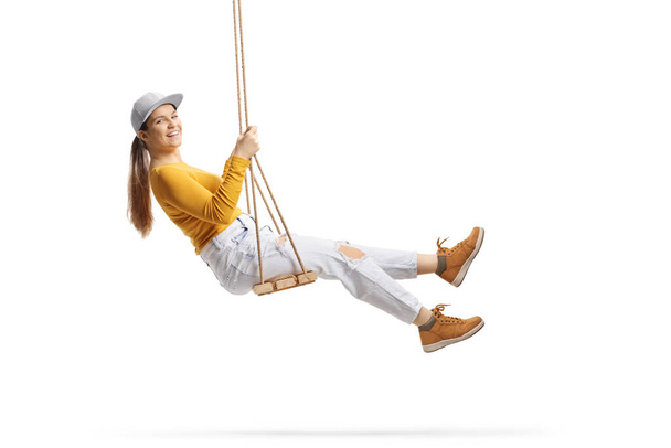 Cheerful female teen swinging on a wooden swing and looking at camera isolated on white background - Foto, Imagem