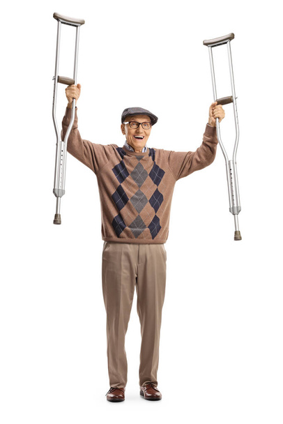 Cheerful elderly man raising crutches and gesturing happiness isolated on white background - Fotó, kép