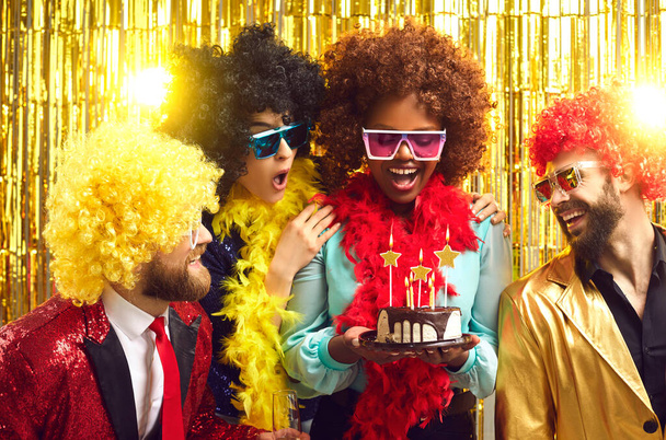 Happy multiracial people in party wigs and bra presenting cake to mate - Photo, image