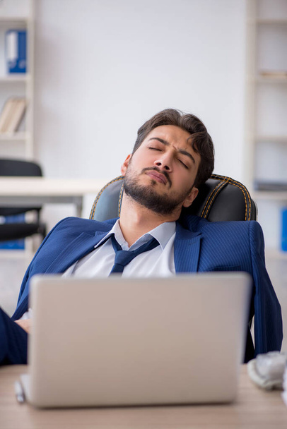 Νεαρός άνδρας υπάλληλος εξαιρετικά κουρασμένος στο γραφείο - Φωτογραφία, εικόνα