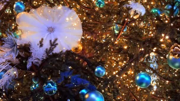 Cierra las luces de un árbol de Navidad brillando por la noche. El abeto de Año Nuevo con adornamientos y la iluminación. Fondo decoraciones árbol de Navidad. Muchas bolas grandes doradas y azules sobre el abeto Año Nuevo y - Imágenes, Vídeo