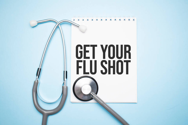Paper with text get your flu shot on blue background with stethoscope and pills - Фото, изображение