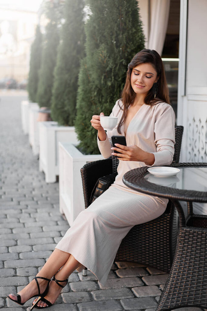 Young beautiful woman with smartphone sitting in the street cafe with coffee. Concept meeting, working, freelance - Foto, Bild
