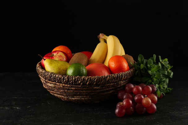 Fresh ripe fruits and wicker bowl on black table - Zdjęcie, obraz