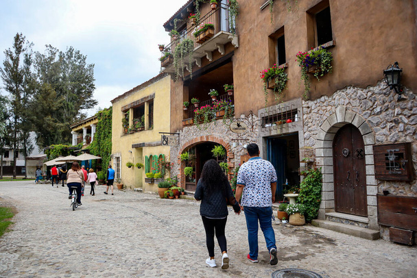 Tlaxcala, Mexico - June 2021: Couple walking through the streets of Val'Quirico, next to houses and buildings with souvenir shops, the streets are adorned with flowers and plants. - Foto, afbeelding