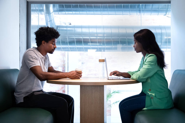 Espacio de coworking. Jóvenes compañeros afroamericanos comparten mesa para trabajar usando laptop. - Foto, Imagen