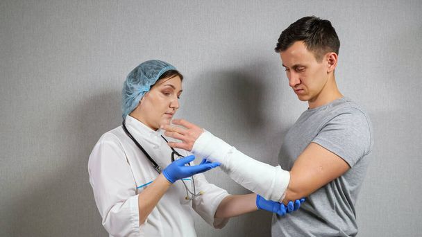 Brunette médecin examine l'avant-bras cassé du jeune homme - Photo, image