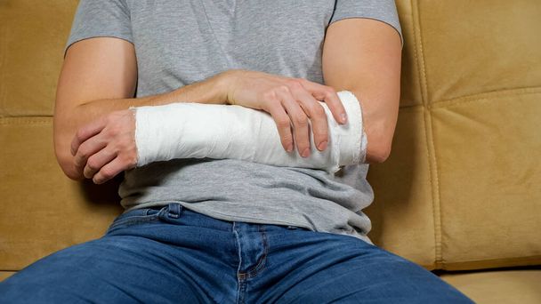 Man touches injured arm in gypsum band and sighs tiredly - 写真・画像