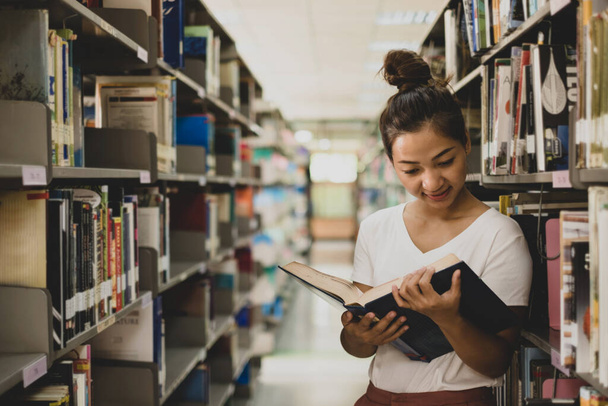 アジアの若い女性たちは、大学図書館の表や通路にある本や本を探し、学術や教育の自己を研究開発しています。. - 写真・画像