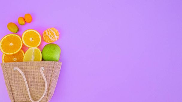 Fresh tropical citrus fruits in hessian shopping bag on violet background message card with copy space for text - Fotoğraf, Görsel