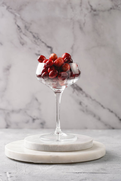 Wide champagne glass filled with fresh raw cranberries on a round marble tray - 写真・画像