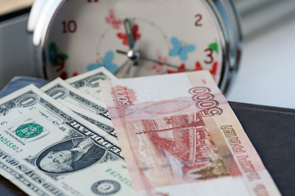ρωσικό και ένα αμερικανικό χρήματα σε ένα φόντο του συναγερμού. ο χρόνος είναι χρήμα - Φωτογραφία, εικόνα