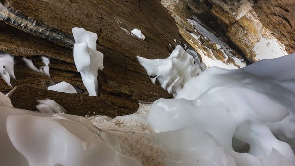 Ледники замерзают в причудливых формах у основания гранитной скалы в пещере. Выход освещен. Сибирь. Байкал. - Фото, изображение