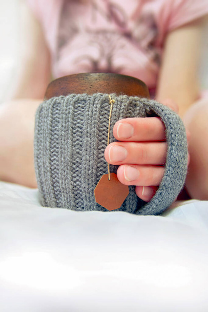 Cozy morning in bed with glanny mug of coffee. Women's hands hold a mug in knitted cover. Close-up. - Fotografie, Obrázek
