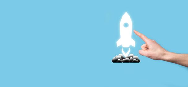 Male hand holding rocket icon that takes off, launch on blue background. rocket is launching and flying out, Business start up, Icon marketing on modern virtual interface.Start up concept - Photo, Image