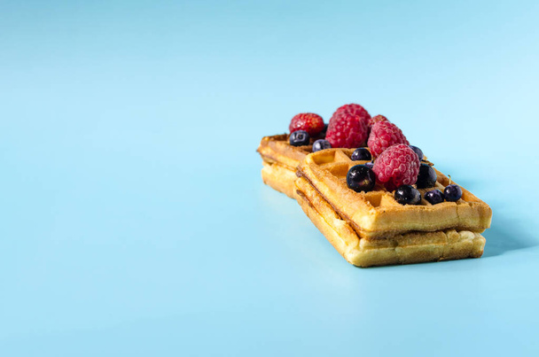 Baking soft waffles with black and red berries on a blue background of bright light. Homemade cakes waffles on a colored background copy space - Foto, afbeelding
