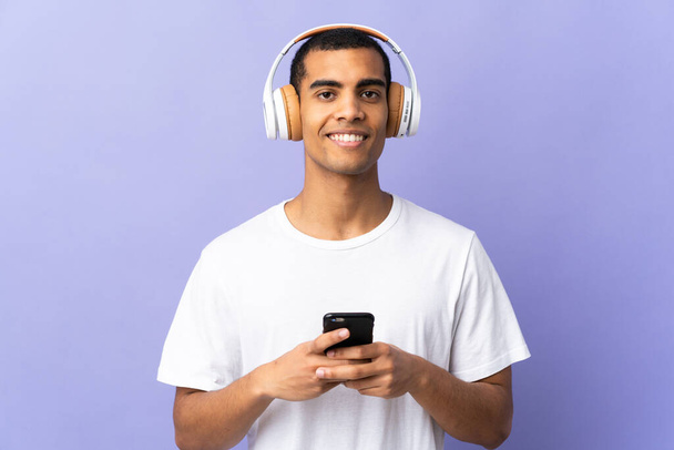 Africký Američan nad izolované fialové pozadí poslech hudby s mobilním a při pohledu dopředu - Fotografie, Obrázek