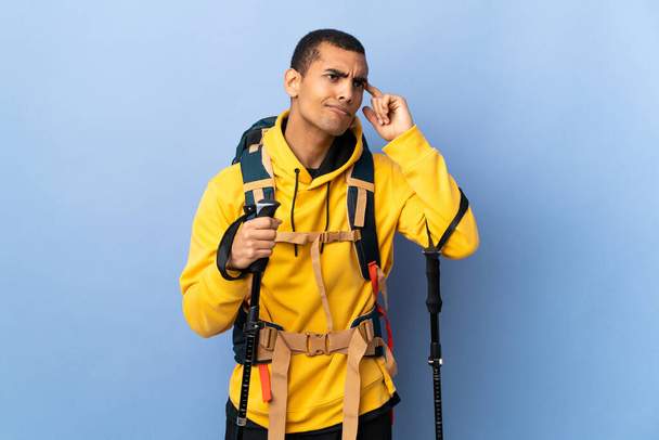 Homem afro-americano com mochila e postes de trekking sobre fundo isolado fazendo o gesto de loucura colocando o dedo na cabeça - Foto, Imagem