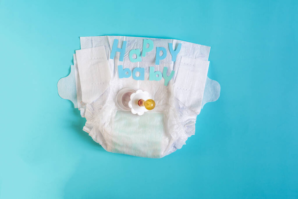 Baby diapers, baby pacifier and the inscription "happy baby" in colored letters on a blue background place for text - Foto, Bild