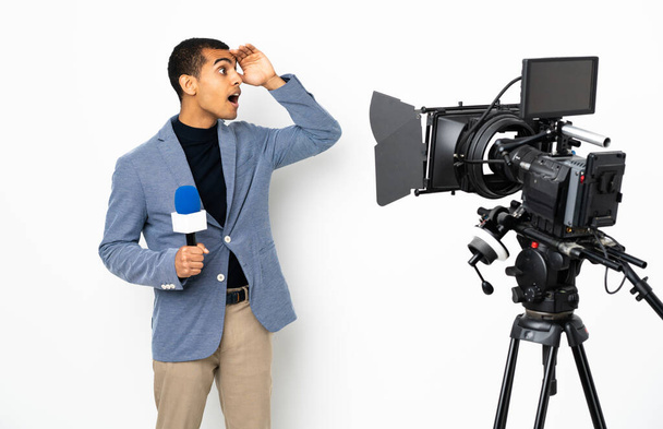 Reporter Afroamerykanin trzyma mikrofon i raportuje wiadomości na odizolowanym białym tle z zaskakującym wyrazem twarzy patrząc w bok - Zdjęcie, obraz