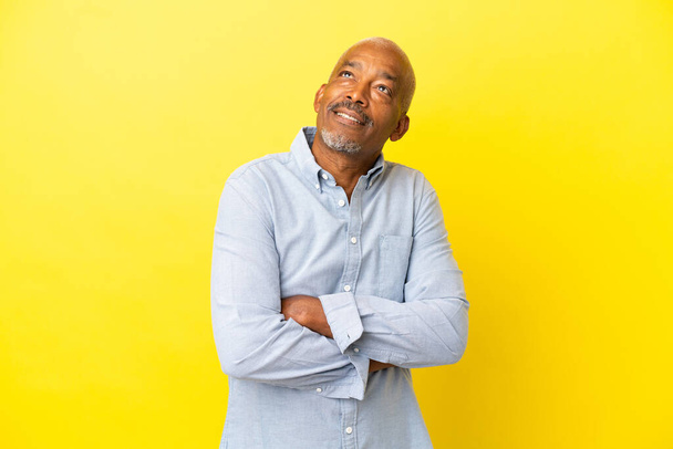 Cuban Senior isolated on yellow background looking up while smiling - Φωτογραφία, εικόνα