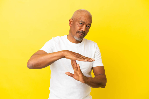 Cuban Senior isolated on yellow background making time out gesture - Photo, Image