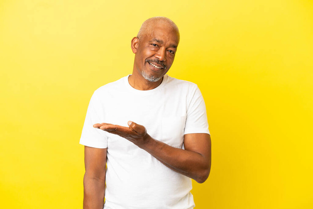 Cuban Senior isolated on yellow background presenting an idea while looking smiling towards - Foto, Imagen