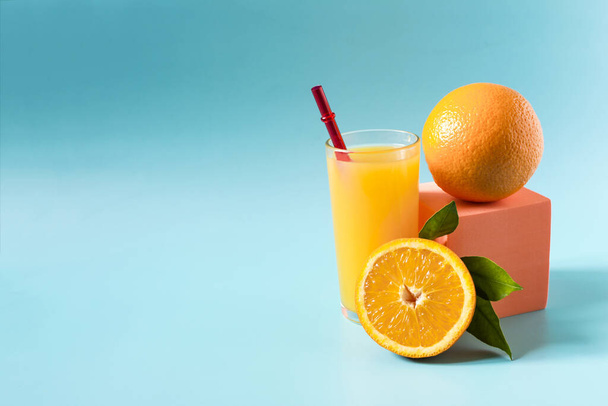 Jugo de naranja en un vaso transparente con una decoración de naranjas y hojas verdes sobre un fondo azul publicidad - Foto, imagen