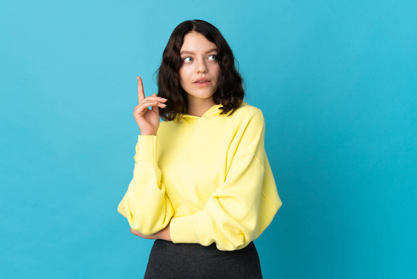 Teenager Ukrainian girl isolated on blue background thinking an idea pointing the finger up - Foto, Imagen