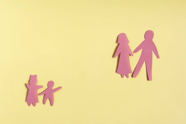 Colored cardboard figures of people of different generations on a yellow background. Figures of separated adults and children color background - Foto, Imagem