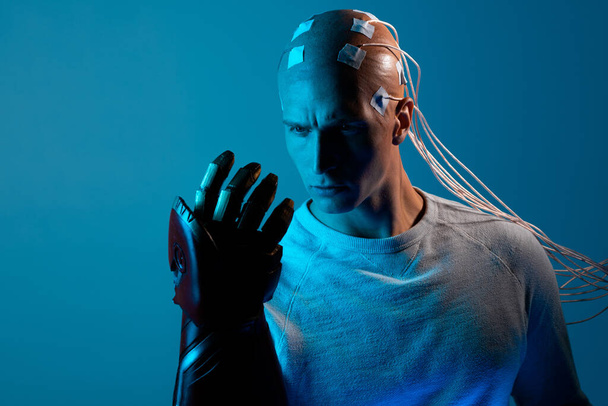 young man with a head entangled with wires and with a robotic arm, - Foto, Bild