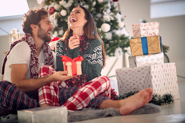 A girl can not hide her excitement because of a christmas present she got from her boyfriend while they are sitting on the floor during christmas holidays in a pleasant atmosphere at home together. Christmas, home, relationship, presents - 写真・画像