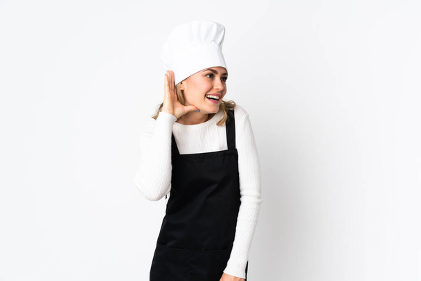 Jonge Braziliaanse chef-kok vrouw geïsoleerd op witte achtergrond luisteren naar iets door het leggen van de hand op het oor - Foto, afbeelding