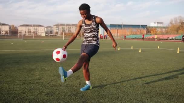 Joven jugador del equipo de fútbol femenino negro entrenando en el estadio de la ciudad y hace malabares con la pelota lanzándola de pie a pie - Metraje, vídeo
