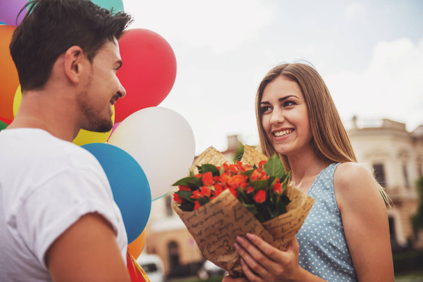 schöner Mann überrascht seine Freundin an ihrem Geburtstag mit bunten Luftballons und Blumen. - Foto, Bild