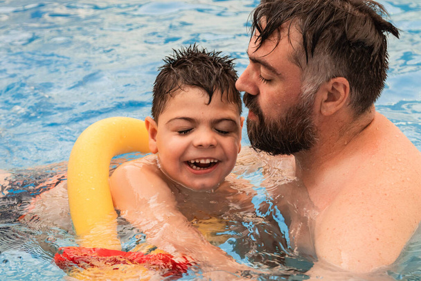 niño discapacitado con una carroza ríe mientras juega y nada en una piscina con su padre - Foto, Imagen