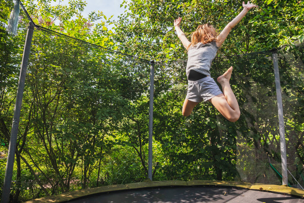 Preteen lány szórakozás pattogó egy trambulin a kertben egy nyári napon - Fotó, kép