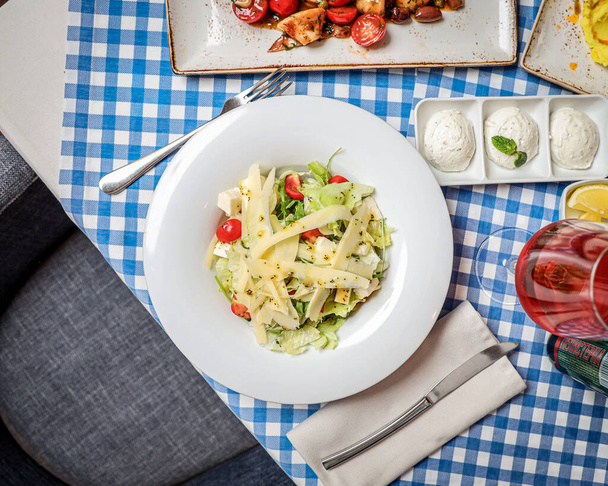 A top view of a salad with cheese and cherry tomatoes on a plate with ingredients and a glass of wine - Foto, immagini