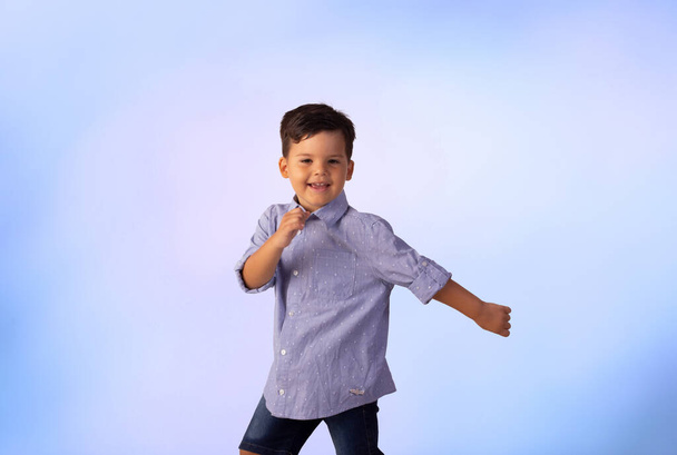 Erkek çocuk stüdyo fotoğrafında mavi arka planda gömlek ve kot pantolon giyiyor.. - Fotoğraf, Görsel
