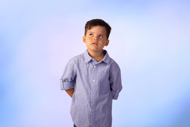 Erkek çocuk stüdyo fotoğrafında mavi arka planda gömlek ve kot pantolon giyiyor.. - Fotoğraf, Görsel