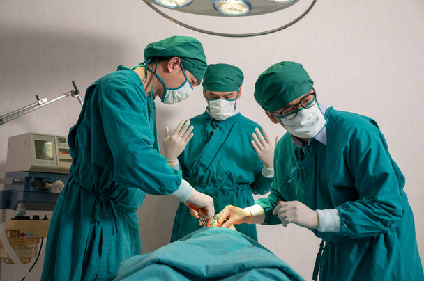 Aasialaiset kirurgit joukkue kirurginen puku suorittaa leikkauksen vakavasti loukkaantunut potilas leikkaussalissa sairaalassa - Valokuva, kuva