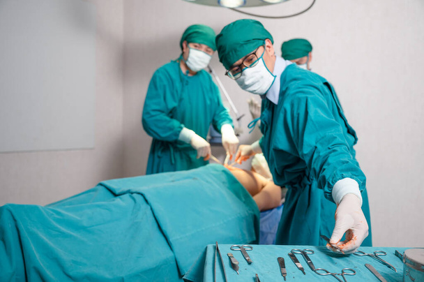 Asiatischer Team-Chirurg greift bei Operation schwer verletzter Patientin im Operationssaal zum Skalpell - Foto, Bild