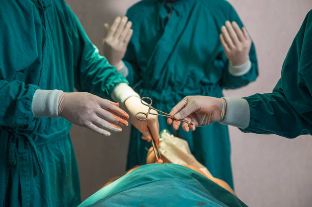 Equipe de cirurgiões realizando cirurgia e passando a tesoura cirúrgica no paciente lesionado no centro cirúrgico do hospital - Foto, Imagem
